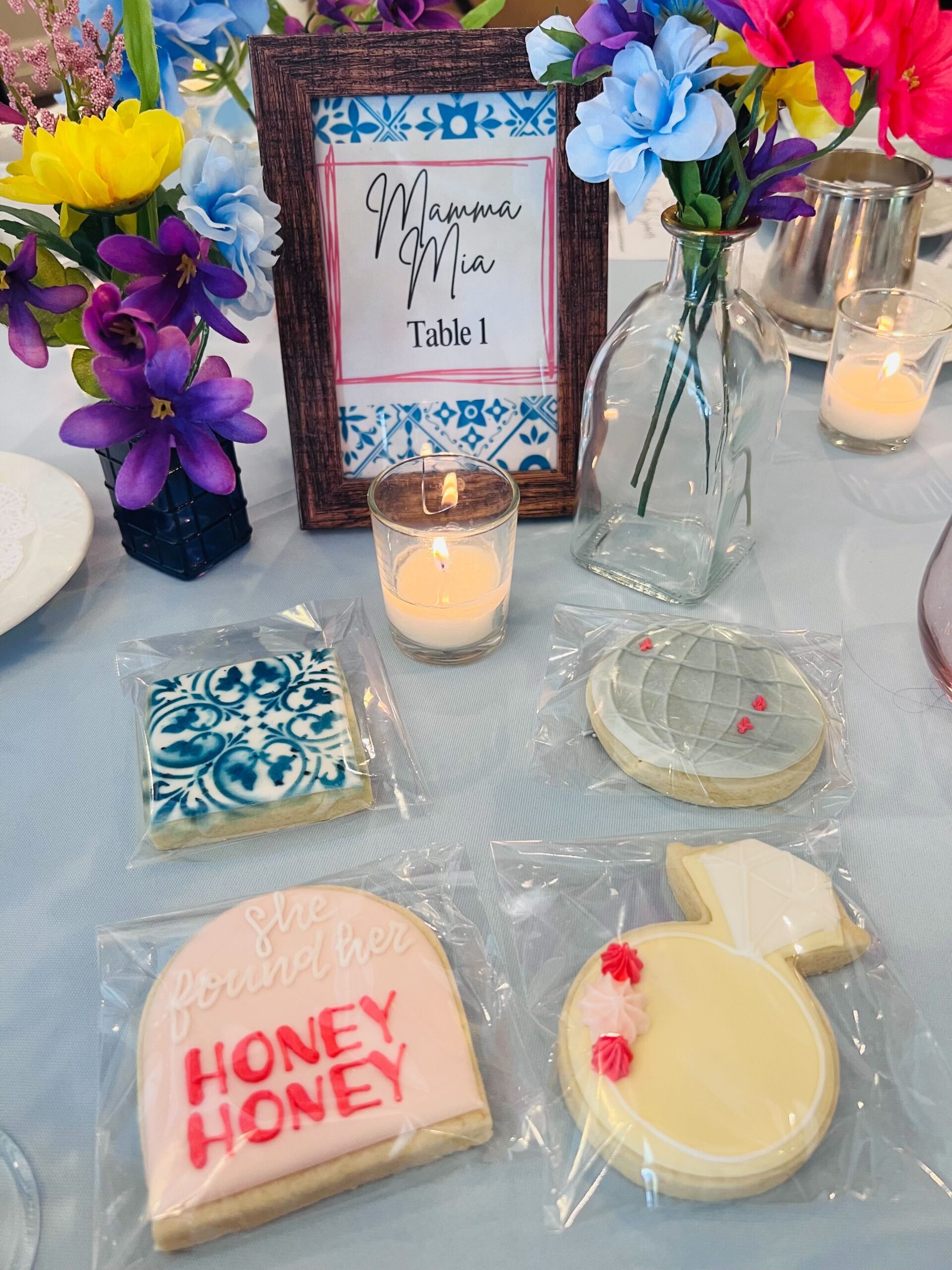 Colorful floral centerpieces and ABBA song-name table signs at a Mamma Mia bridal shower